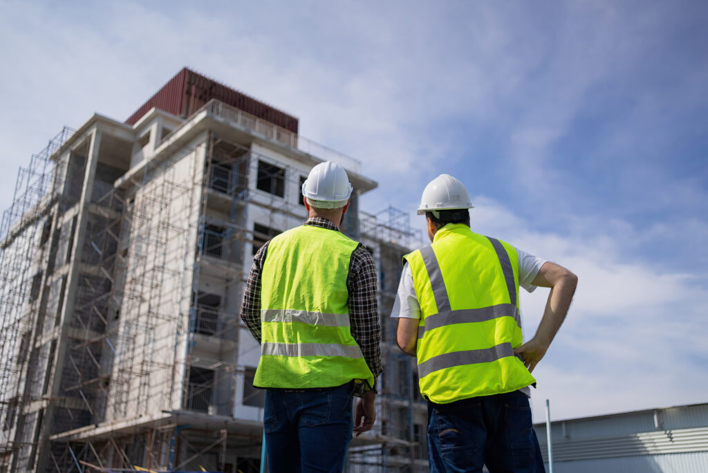 Engineers in hard hats inspect a large building covered in scaffolding.