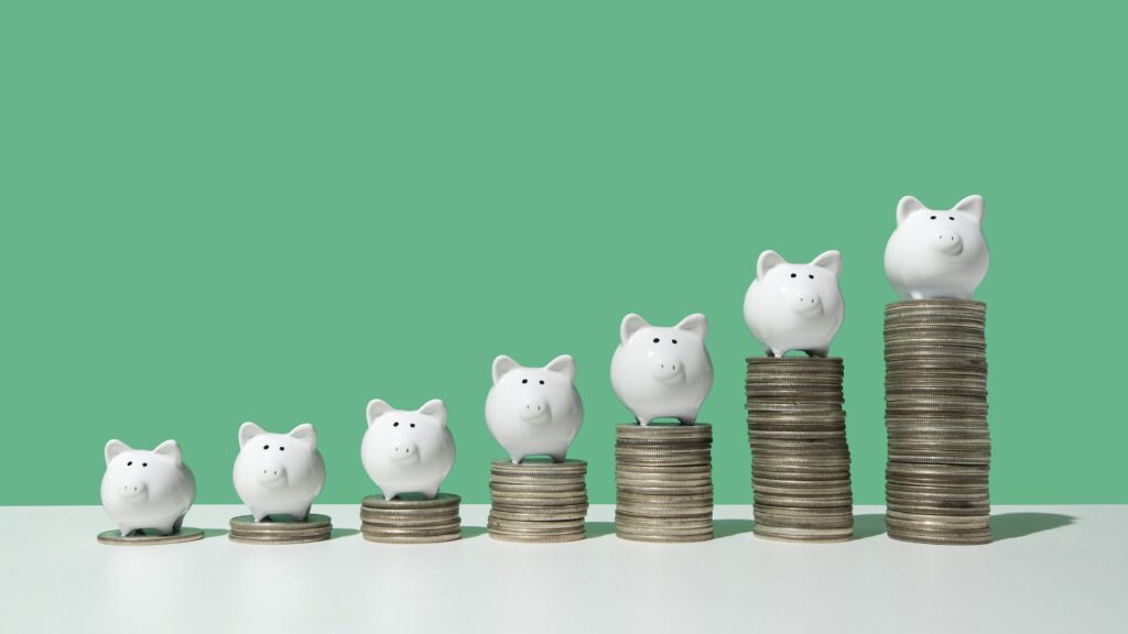 Small piggy banks sit on stacks of coins that get subsequently higher.