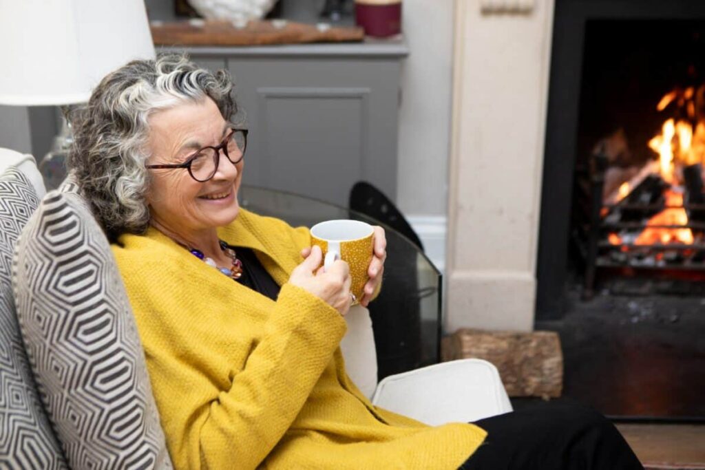 2 UK shares I’d prefer to own over Lloyds stock right now A mature adult sitting by a fireplace in a living room at home. She is wearing a yellow cardigan and spectacles.