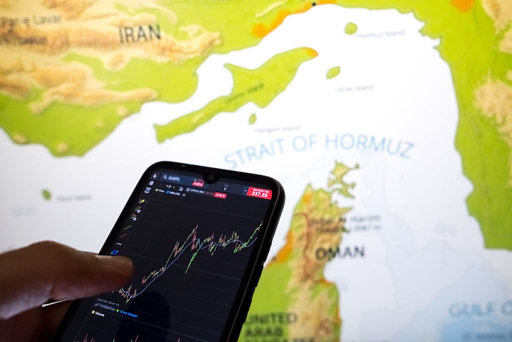 Stocks Edge Up Ahead of Hormuz Deadline: Stock Market Today A stock chart on a smartphone screen with a map of the Strait of Hormuz
