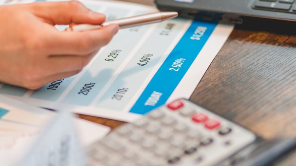 Hand using a calculator to analyze interest rates on a chart