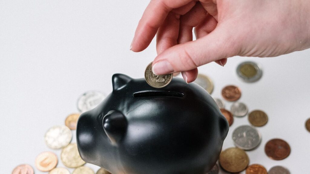 Why More Than Half of Americans Are Living Paycheck to Paycheck in 2026 Hand placing a coin in a piggy bank while living paycheck to paycheck
